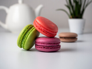 Colorful delicious macaroons lie on a white table. In the background is a white teapot and a flower
