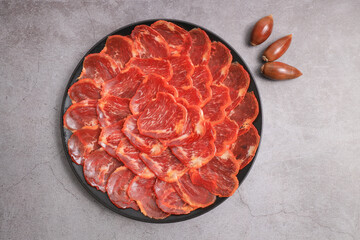 Portion of acorn-fed Iberian loin decorated with acorns on a black plate and with a gray background