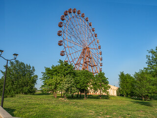 Landscape of a city park with a guard wheel over a yellow building, flowering trees