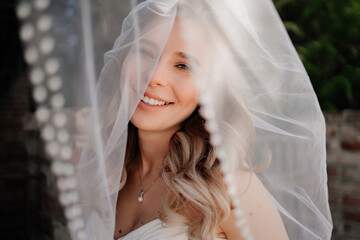 happy bride with long wavy hair under the veil outside. Wedding make-up. 
