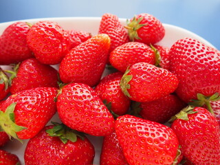 Strawberries on a plate, blue background. White dishes and ripe delicious red large garden...