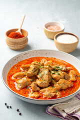 Chicken stew with paprika, onion and sour cream in plate on concrete background. Traditional Hungarian dish Paprikash.