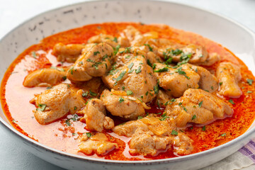 Chicken stew with paprika, onion and sour cream in plate on concrete background. Traditional Hungarian dish Paprikash.