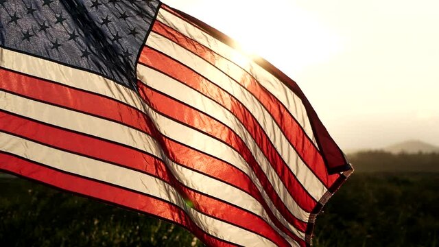 Close-up American flag waving over sunset in nature background, soft focus, Slow Motion. Concept of Memorial Day, 4th of July, Independence Day, Veterans Day, Celebrate USA, United States of American.