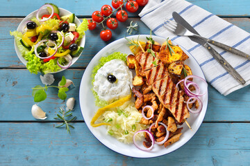 Griechischer Grillteller mit Tzatziki und Krautsalat, dazu ein kleiner Bauernsalat mit Feta –...
