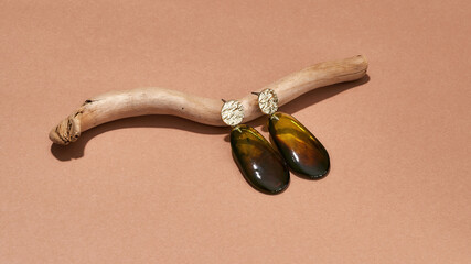 Studio shot of dangle earrings made of golden metal and brown amber epoxy resin on wooden stick...