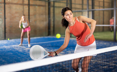 Portrait of sporty adult asian woman playing padel on indoor court, ready to hit ball. Active lifestyle concept.