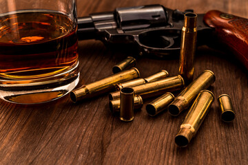 Empty shells from the weapons with glass of whiskey and revolver on a wooden table