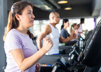 Fototapeta na wymiar Positive girl running on treadmill in fitness club