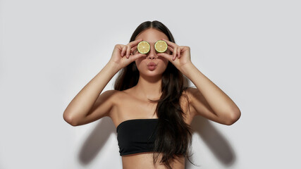 Cheerful young asian girl holding lemon slices near eyes