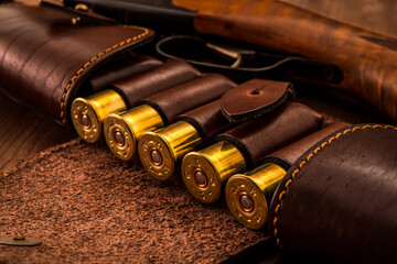 Hunting ammunition 12 gauge in leather bandolier and shotgun on a wooden table. Focus on the...