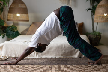 Young african man working out, standing in yoga downward facing dog pose, adho mukha svanasana