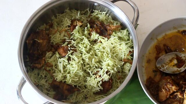 Serving boneless chicken curry and rice layer by layer on to a big bowl to prepare chicken biryani