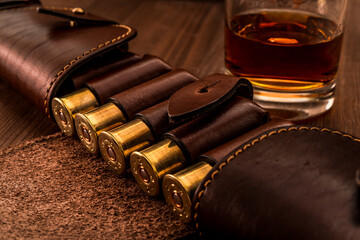 Hunting ammunition 12 gauge in leather bandolier with glass of whiskey on a wooden table. Focus on...