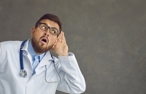 I Can Hear Something Interesting. Portrait Of Funny Curious Doctor On Gray Background Listening With Hand At Ear Overhearing Colleague Talking About Work, Spreading Gossip Or Sharing Amazing Secret