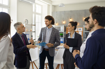 Team of business people standing and talking in office meeting. Experienced senior leader having...