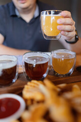 Man sampling variety of seasonal craft beer in pub. Beer samplers in small glasses individually placed in holes fashioned into unique wooden tray. Selective focus with shallow depth of field.