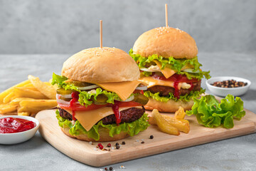 Homemade burgers with beef, cheese and vegetables on a gray background.