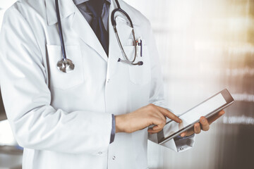 Unknown male doctor using tablet computer in sunny clinic, closeup. Perfect medical service in hospital. Medicine and healthcare concept