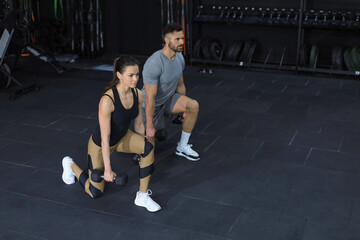 Fototapeta na wymiar Attractive sports people are working out with dumbbells at gym.