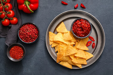 Composition with tasty chili sauce, ingredients and nachos on dark background