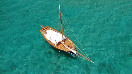 Aerial drone photo of small wooden beautiful sail boat anchored in emerald crystal clear beach of...