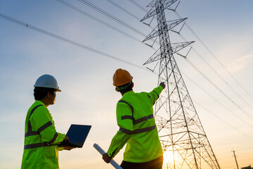 Engineers and Technician working inspections at the electric power station to view the planning work by producing electricity high voltage electric transmission tower at sunset