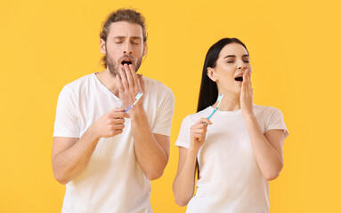 Tired young couple brushing teeth on color background