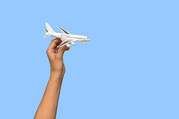 A woman's hand holds a small white airplane in her hand. On a blue background.