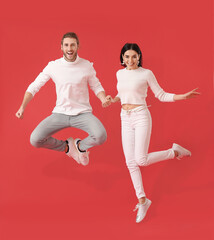 Happy young couple jumping on color background