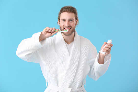 Young man brushing teeth on color background