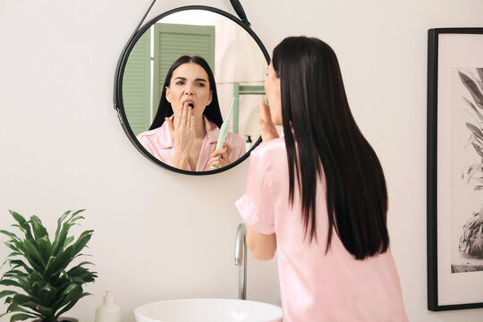 Tired Young Woman Brushing Teeth In Bathroom