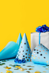 Gift with party cones and confetti on color background