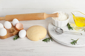 Fresh dough, flour and eggs on light wooden background