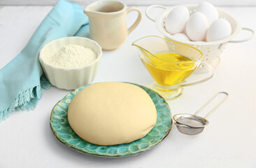 Plate with fresh dough, flour, eggs and oil on light background