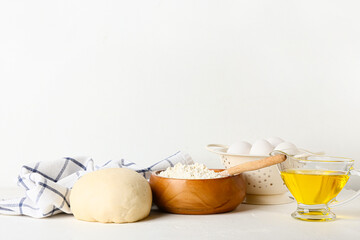 Bowl with fresh dough, flour, eggs and oil on light background