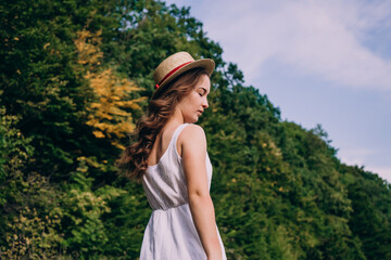 Young woman in a straw hat on a background of green summer forest. Beautiful girl in a dress with a bouquet of dried flowers in the field. Girl in a summer dress.