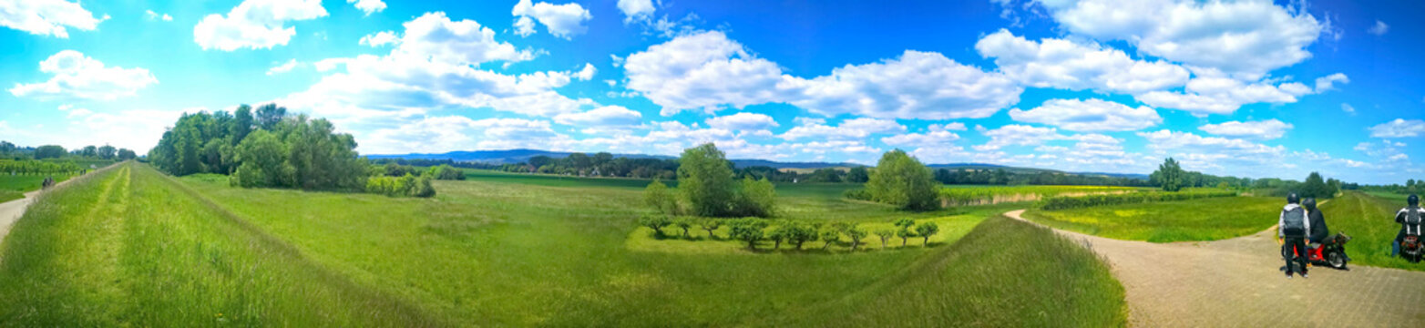 Panoramabild einer grünen Wiese mit Bäumen und blauem Himmel und weißen Wolken.