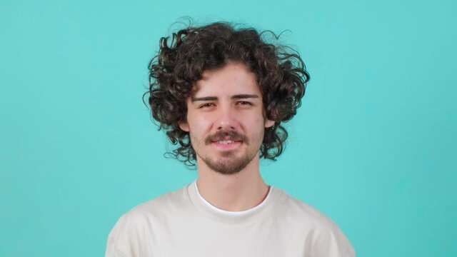 Close up of a curly haired handsome young man that is smiling over turquoise background.