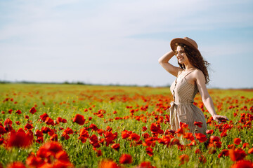 Fototapeta na wymiar Young woman walking in amazing poppy field. Summertime. Beautiful woman posing in the blooming poppy field. Nature, vacation, relax and lifestyle.