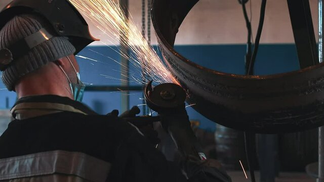 The welder processes the weld with a grinding machine and sparks fly. Processing of welded metal pipe rings. A gas industry welder is practicing the skill of welding pipes.