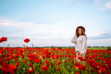 Obraz na płótnie Canvas Young woman walking in amazing poppy field. Summertime. Beautiful woman posing in the blooming poppy field. Nature, vacation, relax and lifestyle.