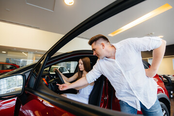 A happy young couple chooses and buys a new car at a car dealership. Buying a new car