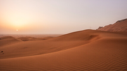 Beautiful desert sunrise with sun visible and sand dooms with sand pattern.