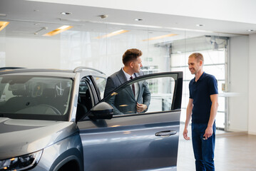 A young businessman with a salesman looks at a new car in a car dealership. Buying a car