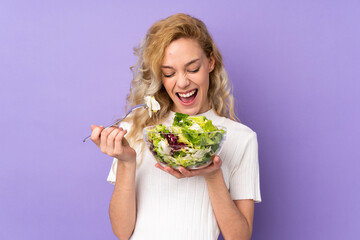 Young blonde woman holding salad isolated on purple background