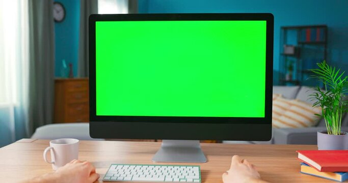 Close up of Male Hand is using computer mouse. Modern Personal Computer with Mock-up Green Screen Display Standing on the Desk of the Cozy Home. POV view of blank computers screen.