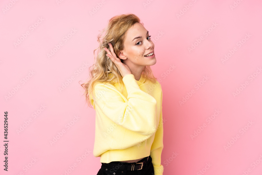 Poster Young blonde woman wearing a sweatshirt isolated on pink background listening to something by putting hand on the ear