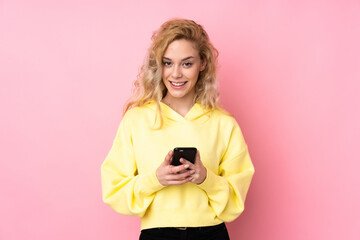 Fototapeta premium Young blonde woman wearing a sweatshirt isolated on pink background sending a message with the mobile