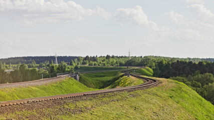 One way railway track turn on green hill on forest trees on horison background, European suburban landscape